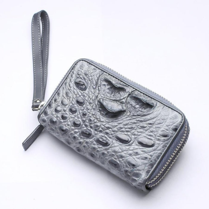 Close-up of genuine gray crocodile hornback leather wallet showing chalky textured bumps, zip-around edge, and attached wrist strap
