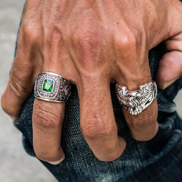 A man's hand wearing the green Spartan ring, resting on jeans.