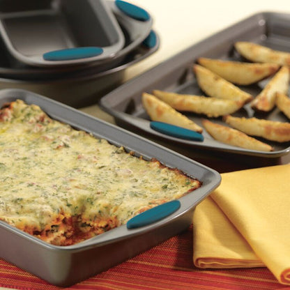 Lasagna and potato wedges rest enticingly in baking trays on a table with a yellow napkin, perfectly cooked in the 5-Piece Nonstick Bakeware Set made of heavy gauge steel, which is oven safe up to 500°F.