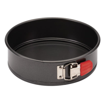 The 9-Inch Nonstick Springform Pan is designed with a black round shape, crafted from heavy gauge steel, and includes a red latch on the side to facilitate easy food release.