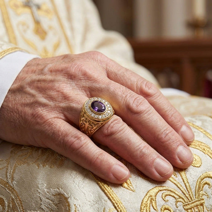Lifestyle view of a hand wearing the yellow gold ring with a deep purple amethyst, resting on embroidered vestments.