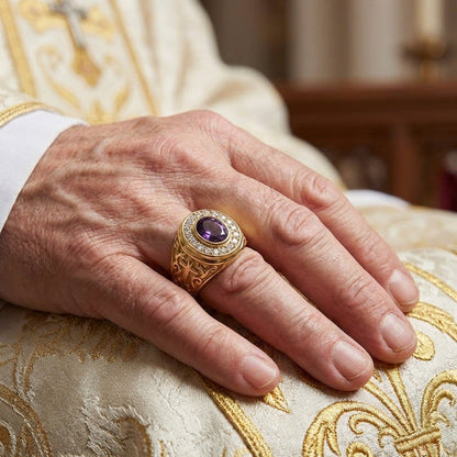 Lifestyle view of a hand wearing the yellow gold ring with a deep purple amethyst, resting on embroidered vestments.