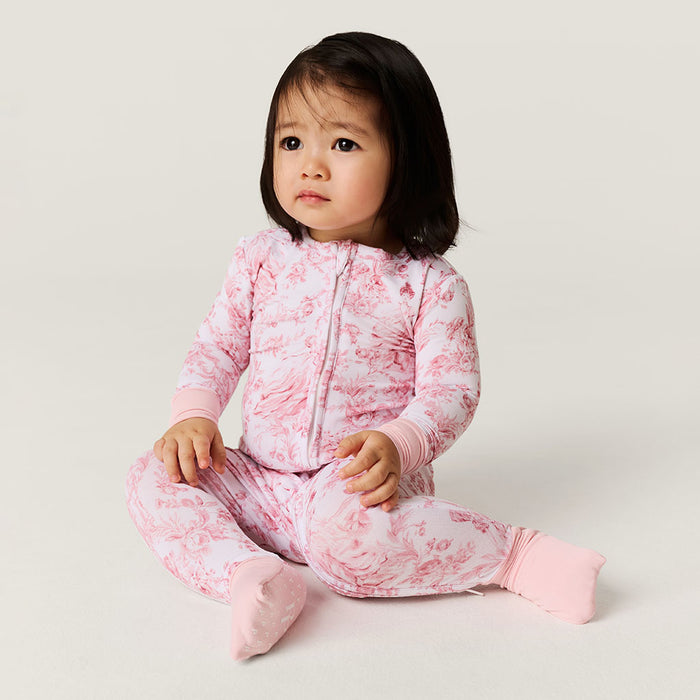 Child wearing a pink one piece outfit on a plain background