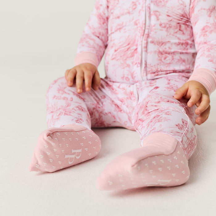 Baby in pink floral one piece sitting on a light background showing detailed footie with brand logo