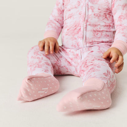 Baby in pink floral one piece sitting on a light background showing detailed footie with brand logo