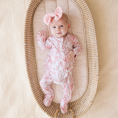 Baby in a floral onesie with a pink bow in a woven basket on a beige background