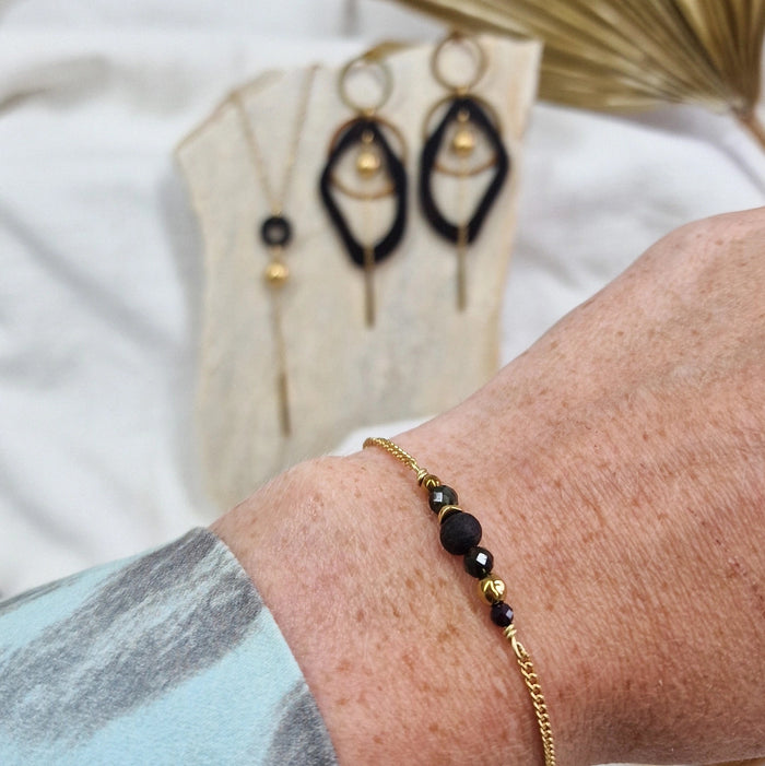Armband aus Räuchereiche mit Holzperlen und goldfarbener Kette am Handgelenk getragen, im Hintergrund passende Ohrringe und Halskette