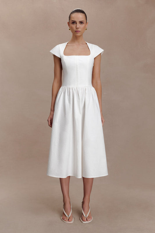 Woman wearing a white dress against a beige background