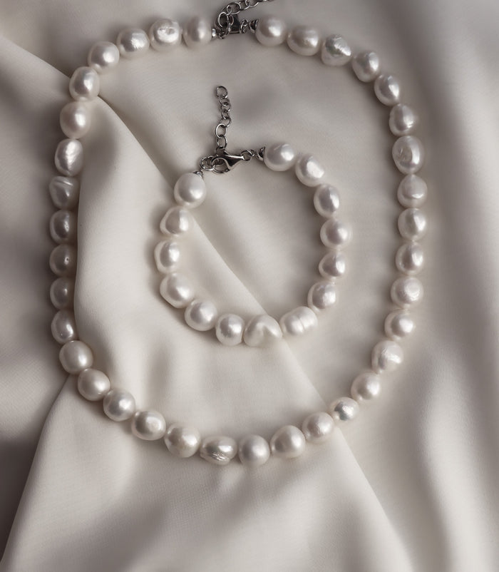 halsband och armband med stora ojämna vita pärlor placerade på ett vitt sidentyg.