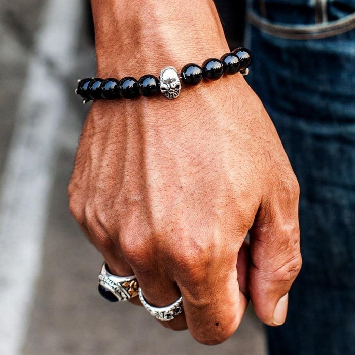 A man's wrist wearing the black onyx beaded skull bracelet, showing the sterling silver skull detail.
