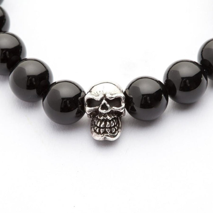 A macro close-up of the detailed, polished sterling silver skull bead set between two black onyx stones.