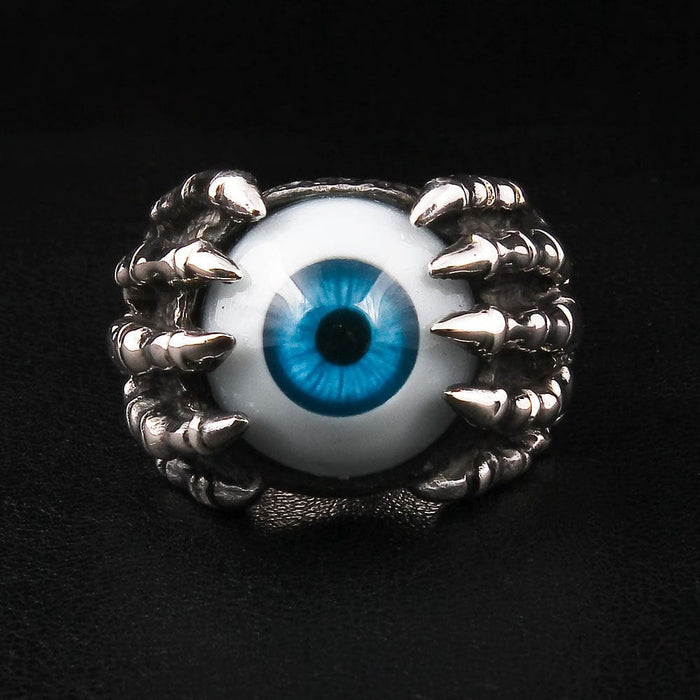 A sterling silver eyeball claw ring with a realistic blue eye held by a skeleton hand, shown on a black background.