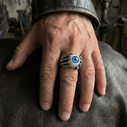 A man's hand wearing the large gothic blue eyeball ring, showing its impressive size and fit.