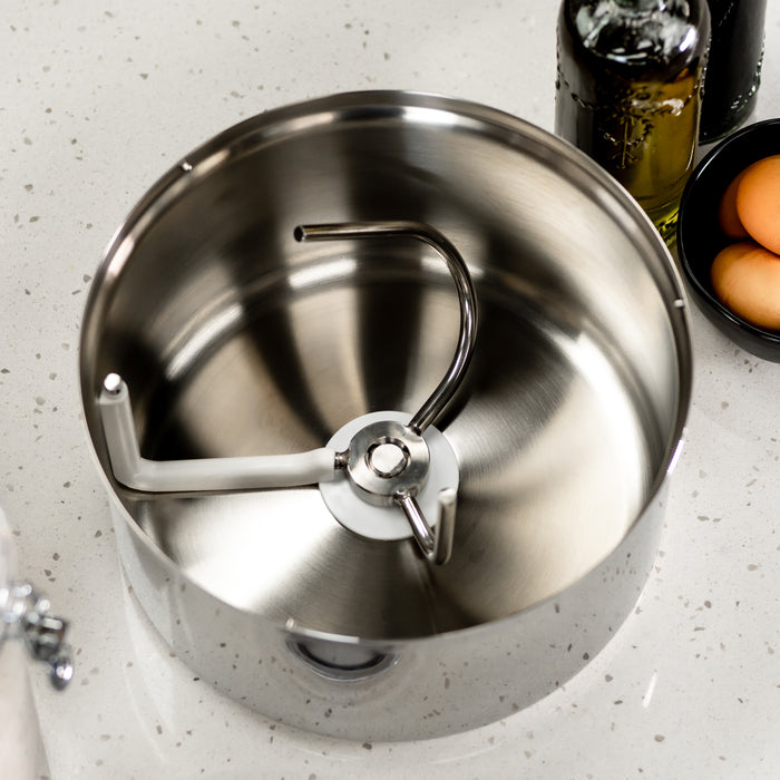 NutriMill bottom drive stainless steel bowl on a white counter next to oil and eggs