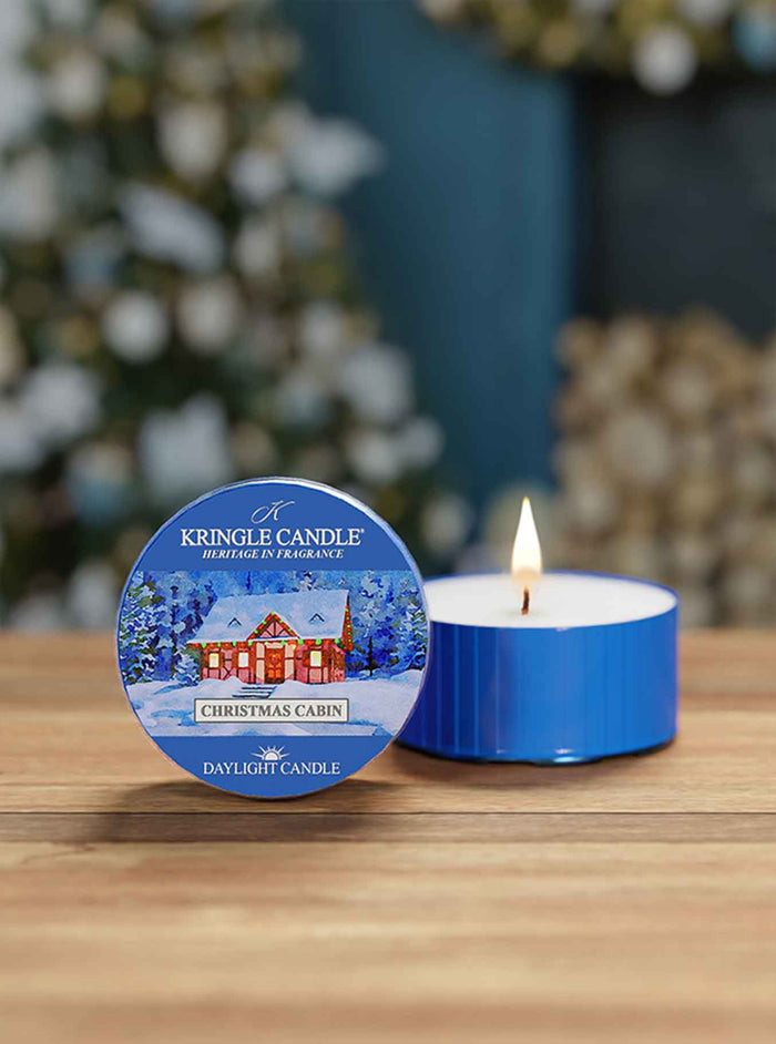 Kingle Candle Christmas Cabin daytime candle on a wooden surface with a blurred festive background