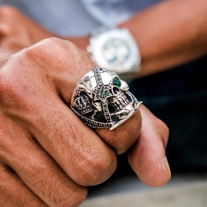 A lifestyle shot of a man wearing the green eye skull ring with a watch in the background.
