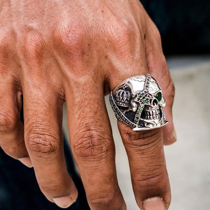 A man's hand wearing the heavy green eye star skull ring on the index finger.