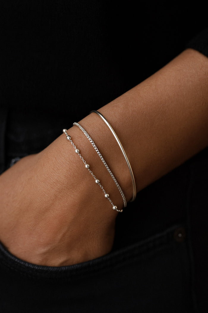 tre silverarmband i kombination på en arm. ett armband med silverkulor, en slät kedja och ett stelt silverarmband.