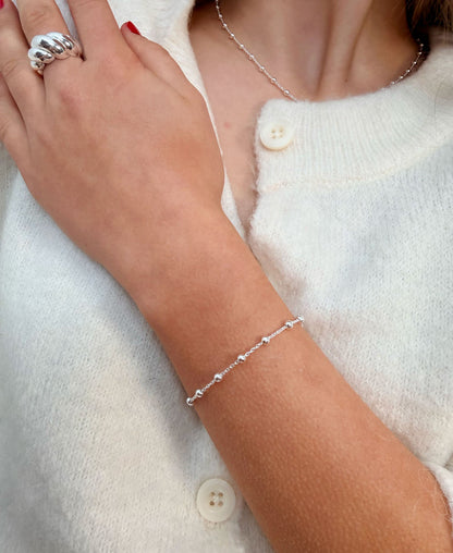 Tjej som bär ett smalt silverarmband med kedja och små kulor tillsammans med matchande halsband och en stor silverring.