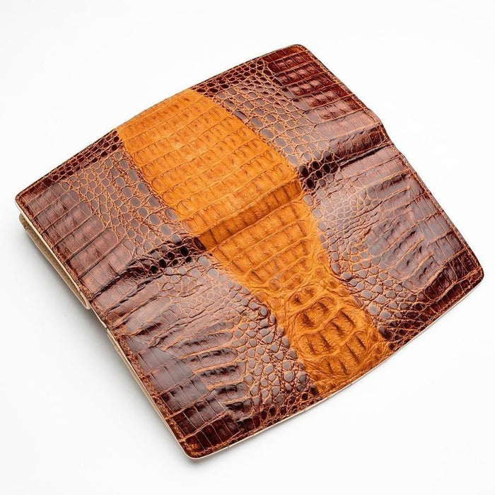 Overhead angled shot of crocodile leather wallet surface showcasing raised brown scutes and golden tan center stripe with natural grain variation