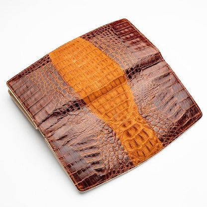 Overhead angled shot of crocodile leather wallet surface showcasing raised brown scutes and golden tan center stripe with natural grain variation
