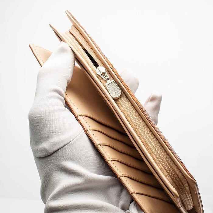 Gloved hand holding crocodile wallet edge open to reveal zippered coin compartment, card slots, and beige leather interior layers
