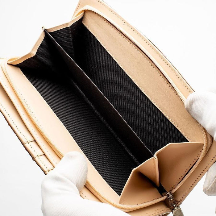Gloved hands holding open gusseted coin section revealing black fabric-lined dual compartments inside beige leather long wallet