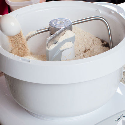 A person pouring ingredients into a white Bosch universal plus mixer