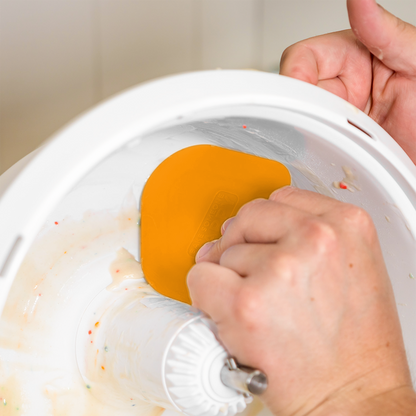 Hand using a NutriMill orange easy scrape bowl scraper to scrape funfetti batter from inside a mixer bowl