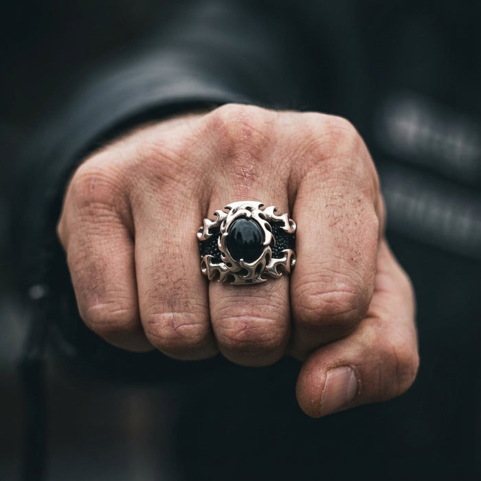 Close-up of a rugged male fist wearing a chunky sterling silver biker ring featuring a flame design, black stingray skin texture, and a central black stone.