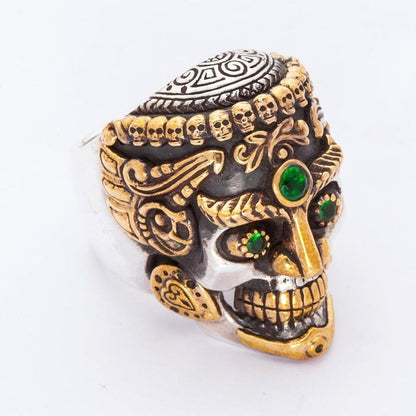 Three-quarter angled view of the silver skull ring showing green stone eyes, gold-tone jaw, and carved mandala cranium.