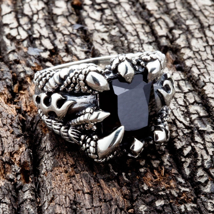 An angled view of the men's gothic dragon claw ring on a wood background, showing the flame and scale band.
