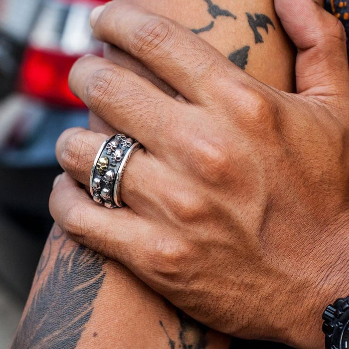 A man's tattooed arm and hand wearing the wide gothic skull spinner ring, showing its bold style.