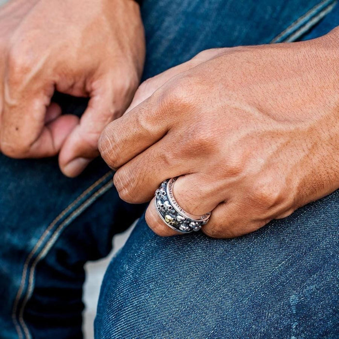 A lifestyle shot of a man wearing the rotating skull band ring while resting his hands on his jeans.