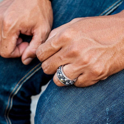 A lifestyle shot of a man wearing the rotating skull band ring while resting his hands on his jeans.