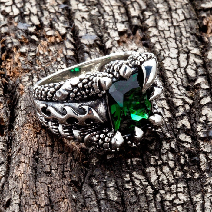 An angled view of the heavy silver emerald claw ring on a dark wood background.