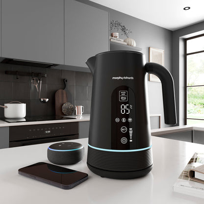 Black Morphy Richards Alexa kettle on a kitchen counter with smartphone and smart speaker.