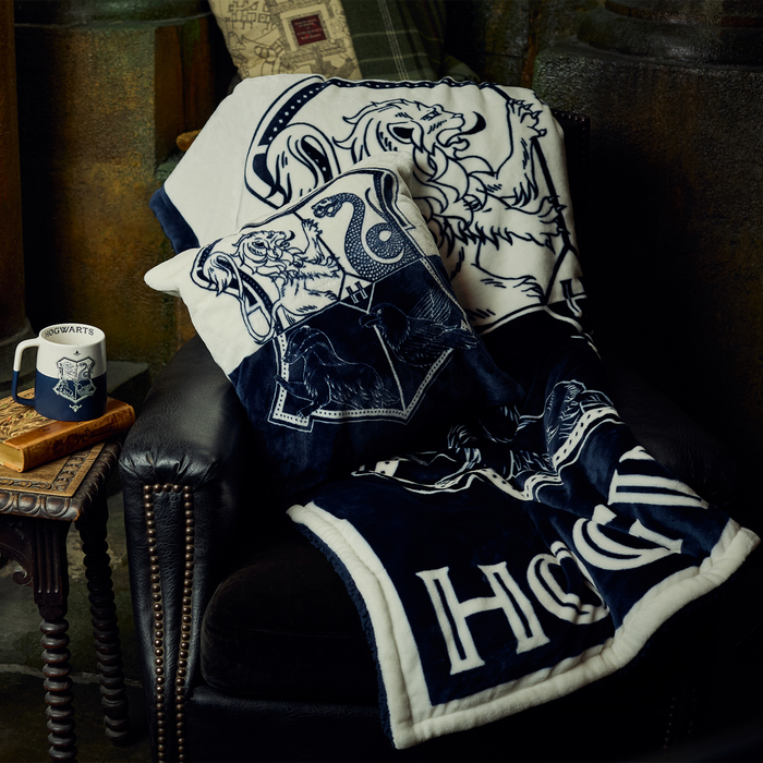 Navy and white blanket with 'Hogwarts' design draped over a chair, next to a mug on a small table.