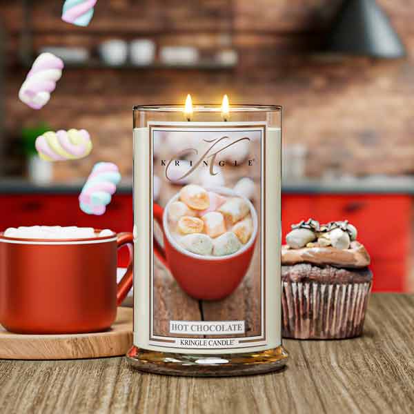 Kringle Candle with hot chocolate design on a wooden table with a cup of hot chocolate and a cupcake.