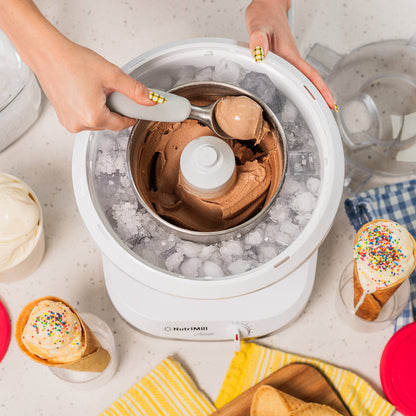 Lifestyle photo of hands using a white ice cream maker with ice cream cones and dishes nearby
