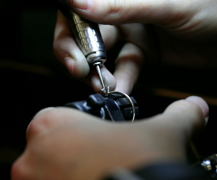 Guldsmed som tillverkare en diamantring och infattar diamanter med ett fattar verktyg.