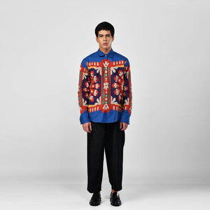 Man wearing the blue Kanaat shirt with black trousers, full length front view, red, navy and orange pattern panel