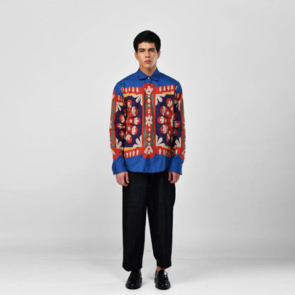 Man wearing the blue Kanaat shirt with black trousers, full length front view, red, navy and orange pattern panel