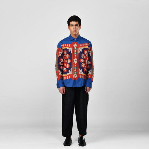 Man wearing the blue Kanaat shirt with black trousers, full length front view, red, navy and orange pattern panel