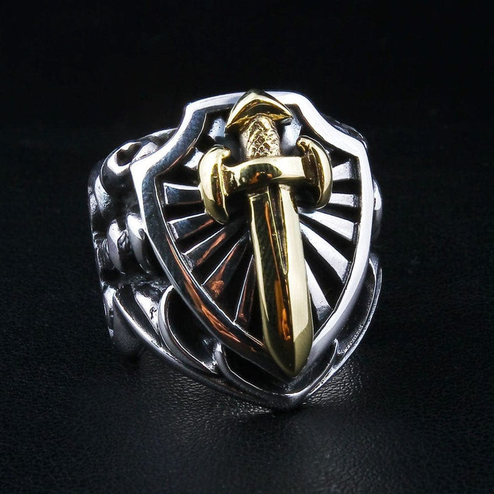 An angled view of the two-tone sword and shield ring on a black leather background.