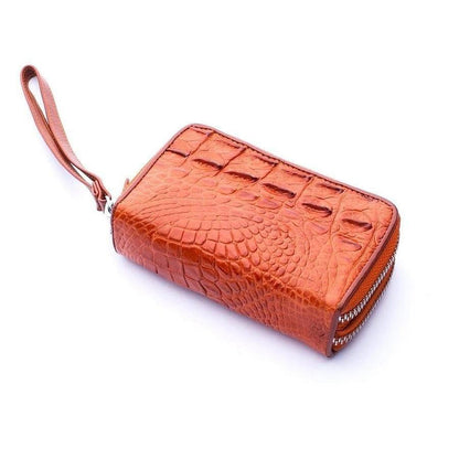 Diagonal view of compact crocodile leather wristlet in warm brown showing prominent raised hornback ridges and silver-tone zipper