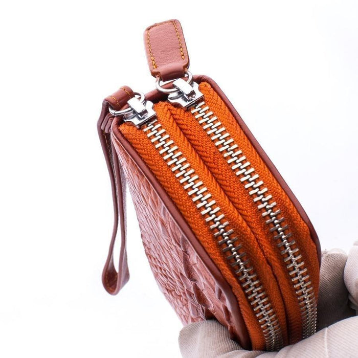 Side view of brown crocodile wallet revealing dual silver-tone zippers with vibrant orange fabric tape and leather pull tab