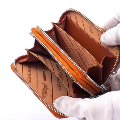 Interior of brown crocodile leather wallet held open with white gloves showing multiple compartments and orange zipper divider