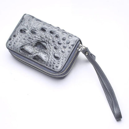Diagonal view of compact gray crocodile leather wallet with dual silver zip-around closures and stitched leather wrist strap