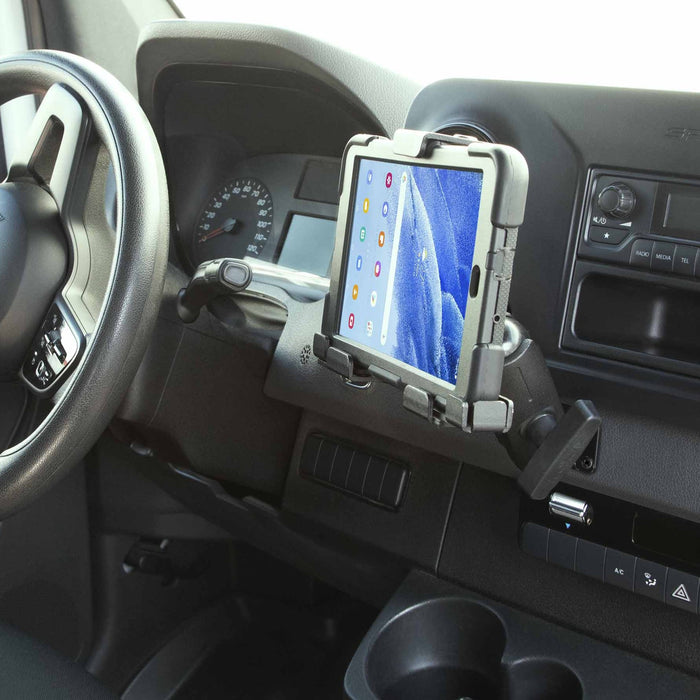 A LockVise™ Metal Locking Tablet Mount with Drill Base Mount and 5″ Metal Shaft is secured to the vehicle’s dashboard, positioned near the steering wheel and instrument panel. The holder supports a tablet displaying app icons on its screen.